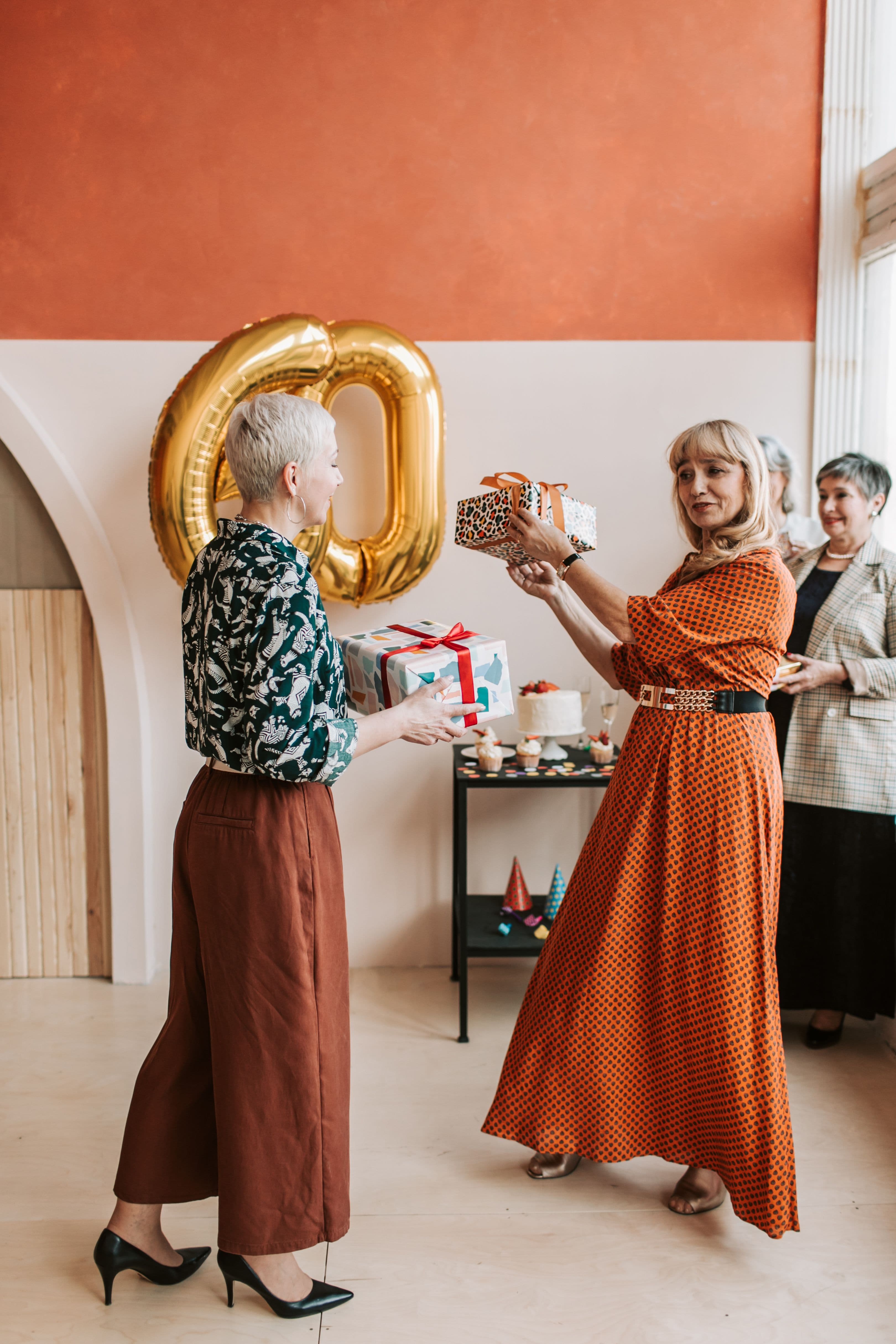 Naiset ojentavat lahjoja merkkipäiväjuhlissa kultaisen 60-ilmapallon edessä